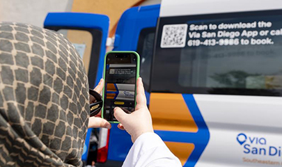 An ethnic woman is taking a picture of a Via San Diego flexible feet van with her cell phone.